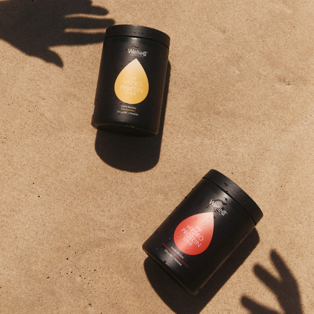 Two black containers with colorful droplet designs on sandy surface.